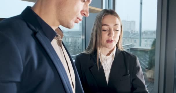 Man and a woman discussing work in the brightly lit modern office. Concerned male and female working with charts papers at hands. Standing business people discuss new startup project concept - Кадри, відео