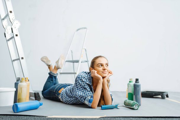 Cheerful female house painter lies on the floor. Home repair, happy woman doing appartment renovation, room decoration renovating - Valokuva, kuva