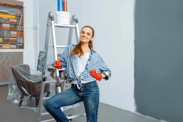 Kobieta malarz domu z ściany farby rolkowe w kolorze szarym. Naprawa domu, śmiejąca się kobieta robi remont mieszkania, renowacja pokoju - Zdjęcie, obraz