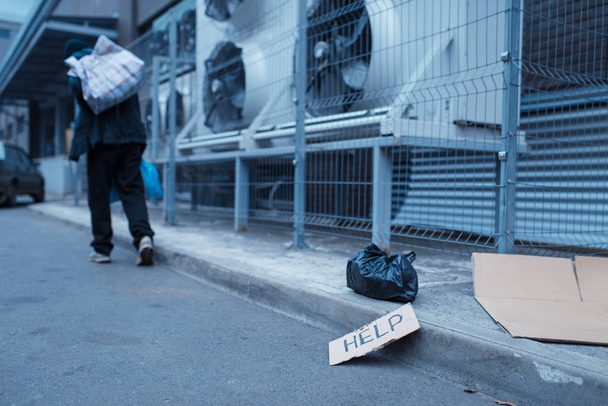 Бездомный и подпись на городской улице. Бедность - социальная проблема, бездомность и одиночество, алкоголизм и пьянство, городской одиночество
 - Фото, изображение
