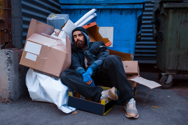 Брудний п'яний жебрак лежить у смітті на смітнику на міській вулиці. Бідність це соціальна проблема, безпритульність і самотність, алкоголізм і п'яна залежність, міське самотнє
 - Фото, зображення