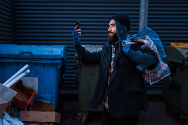 Feliz mendigo encontrado teléfono móvil en basura en la calle de la ciudad. La pobreza es un problema social, la falta de vivienda y la soledad, el alcoholismo y la adicción al alcohol, la soledad urbana
 - Foto, imagen