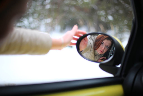 Piękna młoda kobieta z zielonymi oczami i rudymi włosami w żółtym samochodzie w zimowym śnieżnym lesie - Zdjęcie, obraz