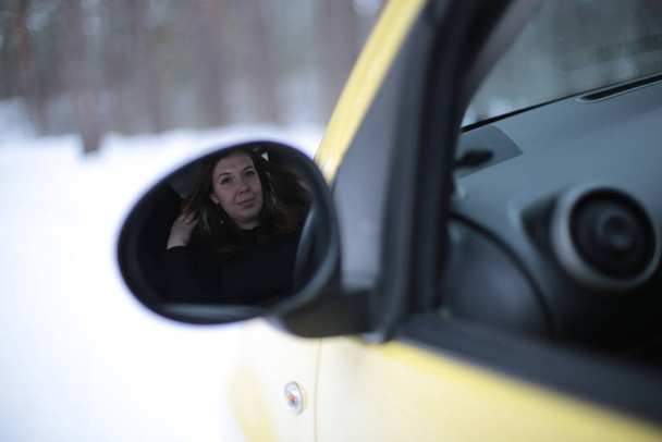 Piękna młoda kobieta z zielonymi oczami i rudymi włosami w żółtym samochodzie w zimowym śnieżnym lesie - Zdjęcie, obraz