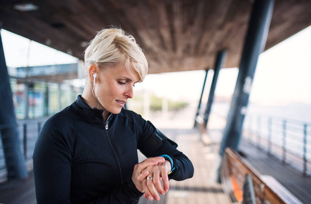 A portrait of young sportswoman with smartwatch outdoors, self-tracking. - Zdjęcie, obraz