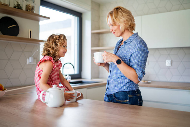 A cute small girl with mother indoors in kitchen at home. - Φωτογραφία, εικόνα