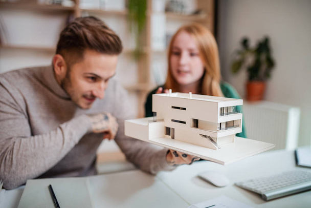 Architects with model of house sitting at the desk indoors in office, working. - Fotó, kép