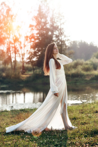 Bela mulher esbelta em um vestido branco longo caminha na morni
 - Foto, Imagem
