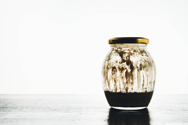 Entrada de massa de farinha de pão em um jarro de vidro em uma mesa contra o fundo branco
 - Foto, Imagem