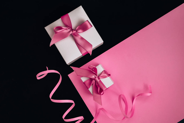 Present boxes with pink ribbon on the pink and black background - Photo, Image