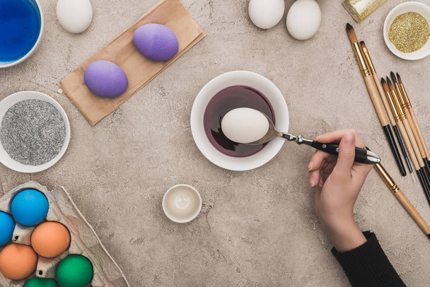 oříznutý pohled ženy zbarvení kuřecích vajec v akvarelech barvy na šedém betonovém povrchu - Fotografie, Obrázek