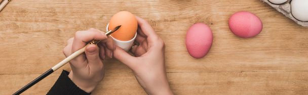 Paskalya yumurtalarını tahta masada fırçayla boyayan kadın manzarası, panoramik çekim. - Fotoğraf, Görsel