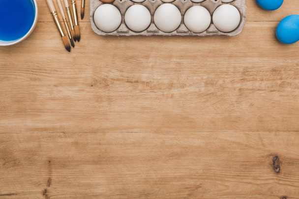 vista dall'alto della vernice ad acquerello blu in ciotola vicino alle uova di pollo e pennelli sul tavolo di legno
 - Foto, immagini