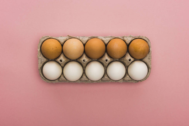 top view of chicken eggs in cardboard box on pink background - Foto, Bild