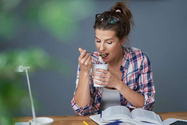 Głodny student jedząc makaron podczas nauki w domu - Zdjęcie, obraz