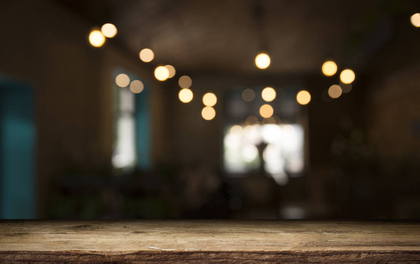 leere Holztischplatte auf unscharfem hellgoldenem Bokeh des Cafe-Restaurants vor dunklem Hintergrund - Foto, Bild