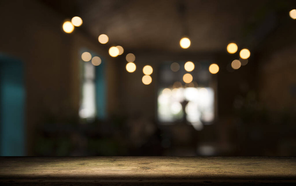 leere Holztischplatte auf unscharfem hellgoldenem Bokeh des Cafe-Restaurants vor dunklem Hintergrund - Foto, Bild