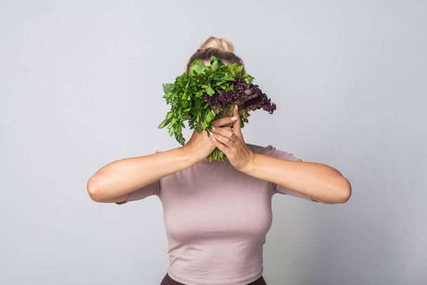 Young woman hiding face behind bunch of herbs, leafy green veget - Photo, Image