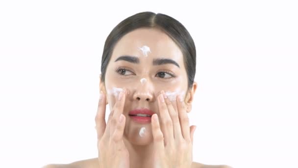 Beauty concept. Beautiful girl is happily applying cream on her face on a white background. 4k Resolution. - Séquence, vidéo