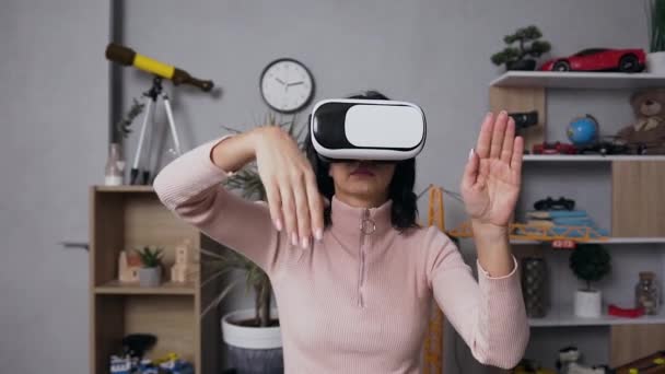 Beautiful focused young woman in casual clothes sitting at the workplace at home and doing different hands movements in air using virtual 3d glasses - Felvétel, videó