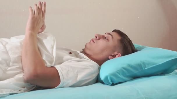 De jonge duizendjarige man gaat in close-up naar bed, zet een alarm op zijn mobiele telefoon voordat hij naar bed gaat. slaapt - Video