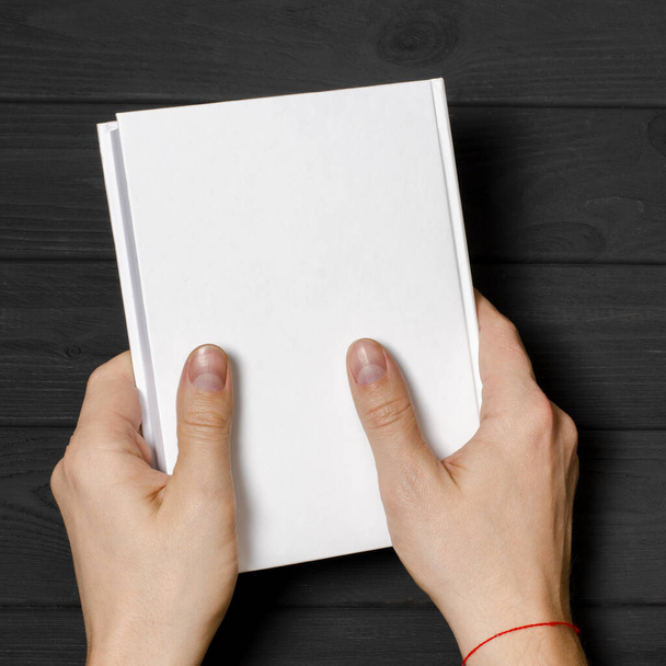 Мужские руки держат закрытую книгу с чистым чехлом на светлом фоне
 - Фото, изображение