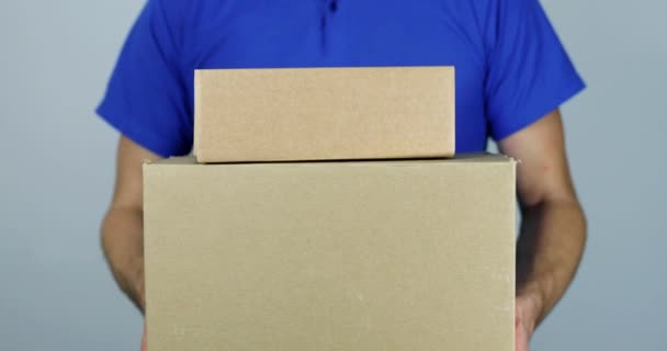 repartidor hombre sosteniendo pila de cajas de cartón en frente sobre fondo gris
 - Metraje, vídeo