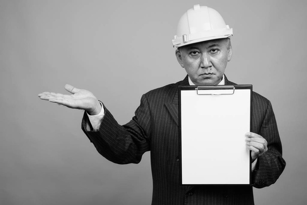 Studio shot of mature Asian businessman as engineer with hardhat against gray background in black and white - Zdjęcie, obraz