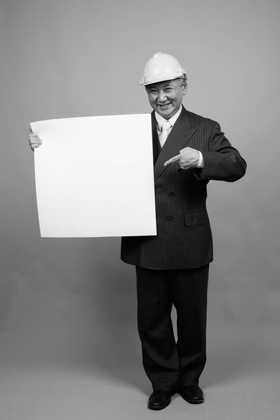 Studio shot of mature Asian businessman as engineer with hardhat against gray background in black and white - Foto, Imagem