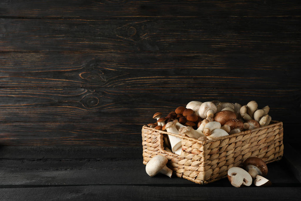 Different mushrooms in basket on wooden background, space for te - Fotoğraf, Görsel