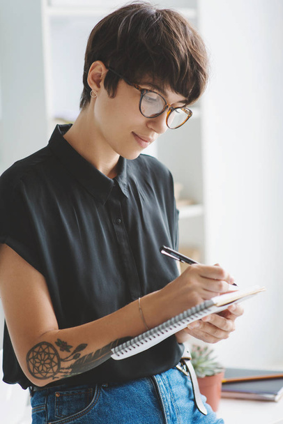 Portrait of young business woman in glasses taking notes in notebook. - Fotó, kép