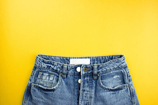 Jeans unisex blu con etichetta bianca posato piatto su sfondo giallo con spazio copia per testo, logo. Vestiti moda tutti i giorni in stile minimal. Modello banner, mockup per web, pubblicità, social media
. - Foto, immagini