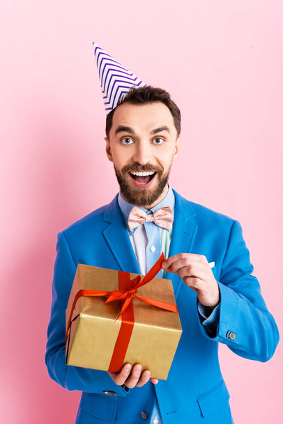 excited businessman in suit holding present on pink  - Foto, Bild