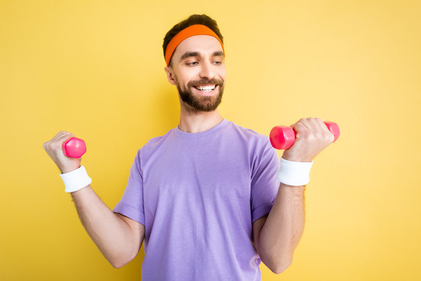 cheerful sportsman exercising with small dumbbells isolated on yellow - Foto, immagini