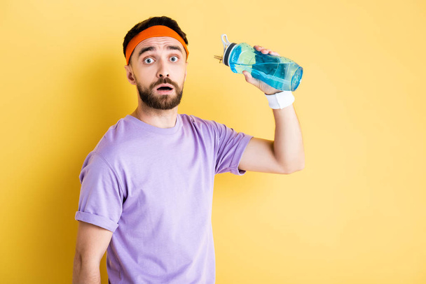 worried sportsman holding sports bottle with water on yellow - Foto, afbeelding