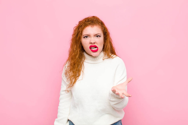 young red head woman looking angry, annoyed and frustrated screaming wtf or whats wrong with you against pink wall  - Фото, зображення