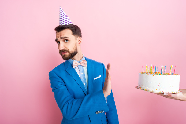 vista recortada de la mujer sosteniendo pastel de cumpleaños cerca de hombre de negocios que muestra ningún gesto en rosa
  - Foto, Imagen