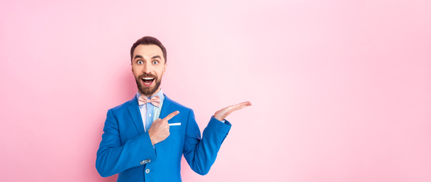 panoramic shot excited man in suit pointing with finger on pink  - Foto, afbeelding