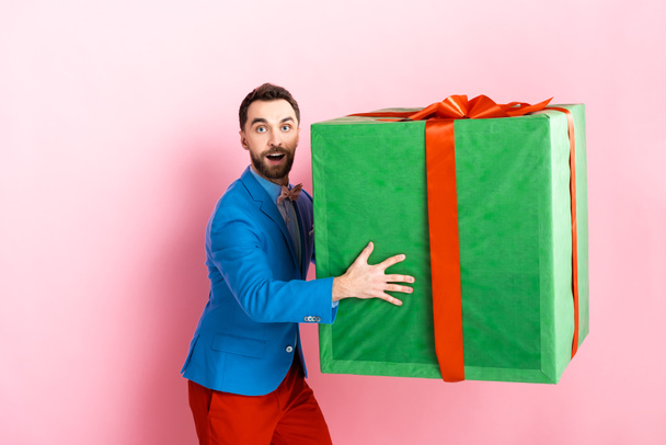 surprised businessman holding huge gift box on pink  - Fotoğraf, Görsel