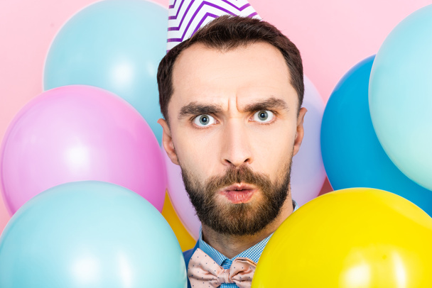 surprised bearded man looking at camera near balloons isolated on pink  - Foto, immagini