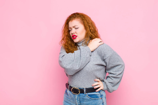 young red head woman feeling tired, stressed, anxious, frustrated and depressed, suffering with back or neck pain against pink wall - Фото, зображення