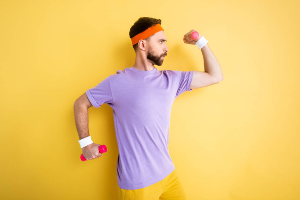 side view of sportsman working out with pink dumbbells on yellow - Fotografie, Obrázek