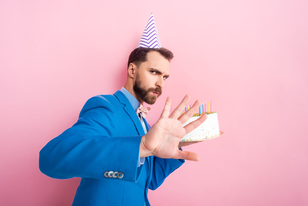 barbudo hombre mostrando ningún gesto mientras sostiene pastel de cumpleaños aislado en rosa
  - Foto, Imagen