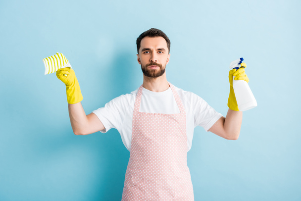 bearded man holding rag and spray bottle for cleaning on blue   - Фото, зображення