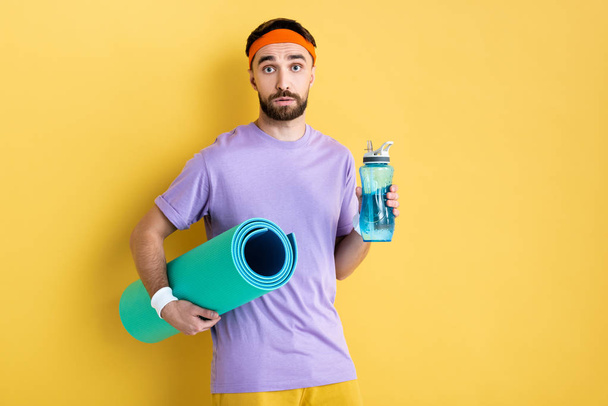  bearded man holding sports bottle and fitness mat on yellow - Fotografie, Obrázek