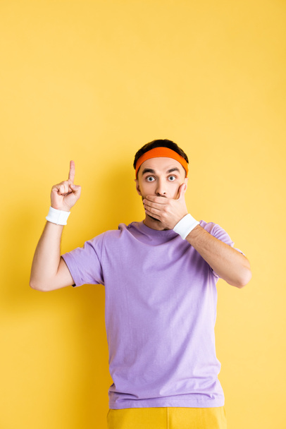 shocked sportsman covering mouth and pointing with finger on yellow - 写真・画像