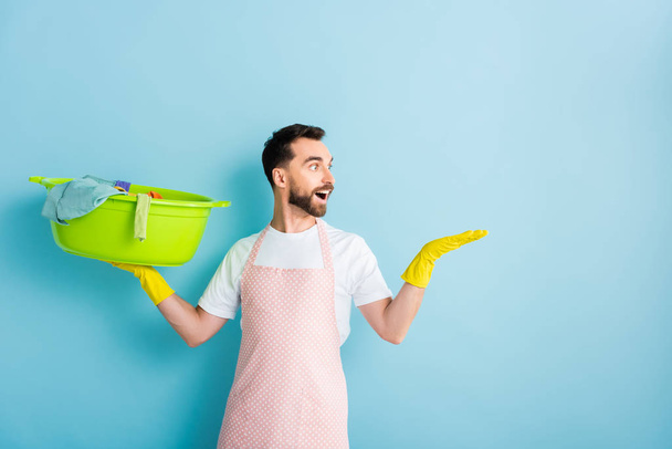 excited bearded man holding dirty laundry and pointing with hand on blue  - 写真・画像