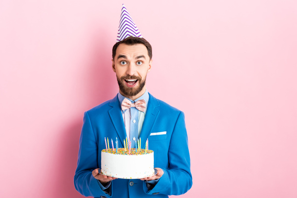cheerful businessman holding birthday cake with candles on pink  - Foto, Bild