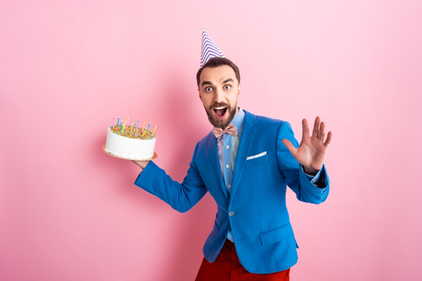vzrušený podnikatel drží narozeninový dort a dívá se na kameru na růžové  - Fotografie, Obrázek