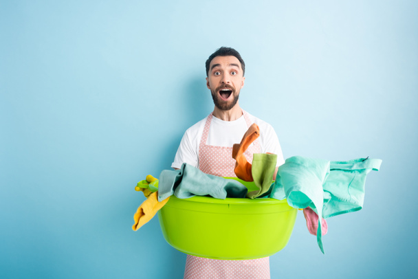 surprised man holding plastic wash bowl with dirty laundry on blue  - Photo, image